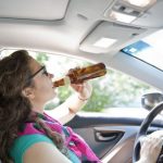 young woman drinking beer in her car